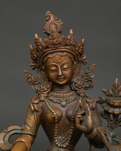 Green Tara statue face with serene expression five jewel crown and lotus.