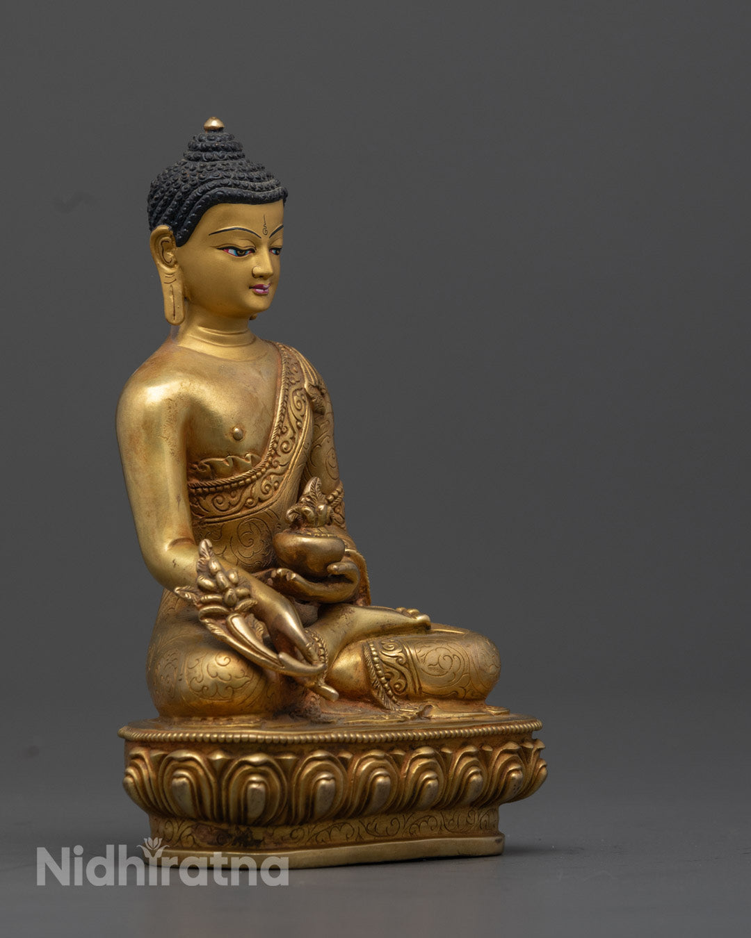 the 24K Gold-Gilded Medicine Buddha Statue, highlighting the detailed carvings on the robe, the myrobalan plant in the left hand, and the vessel of medicinal nectar in the right, with a graceful lotus throne