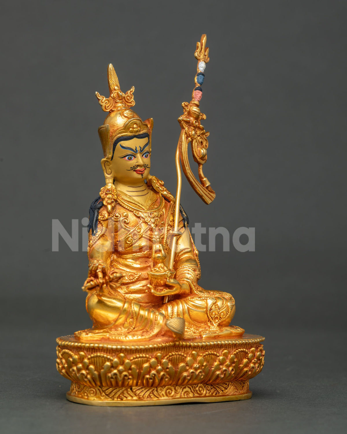 Three-quarter side view of gold Guru Rinpoche statue seated on lotus base holding skull cup