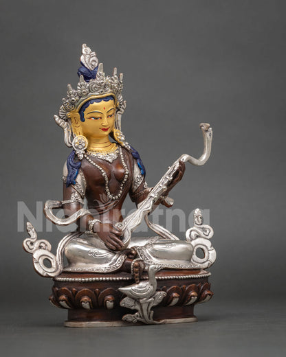 Three-quarter side view of Saraswati statue holding veena, with silver swan on lotus base