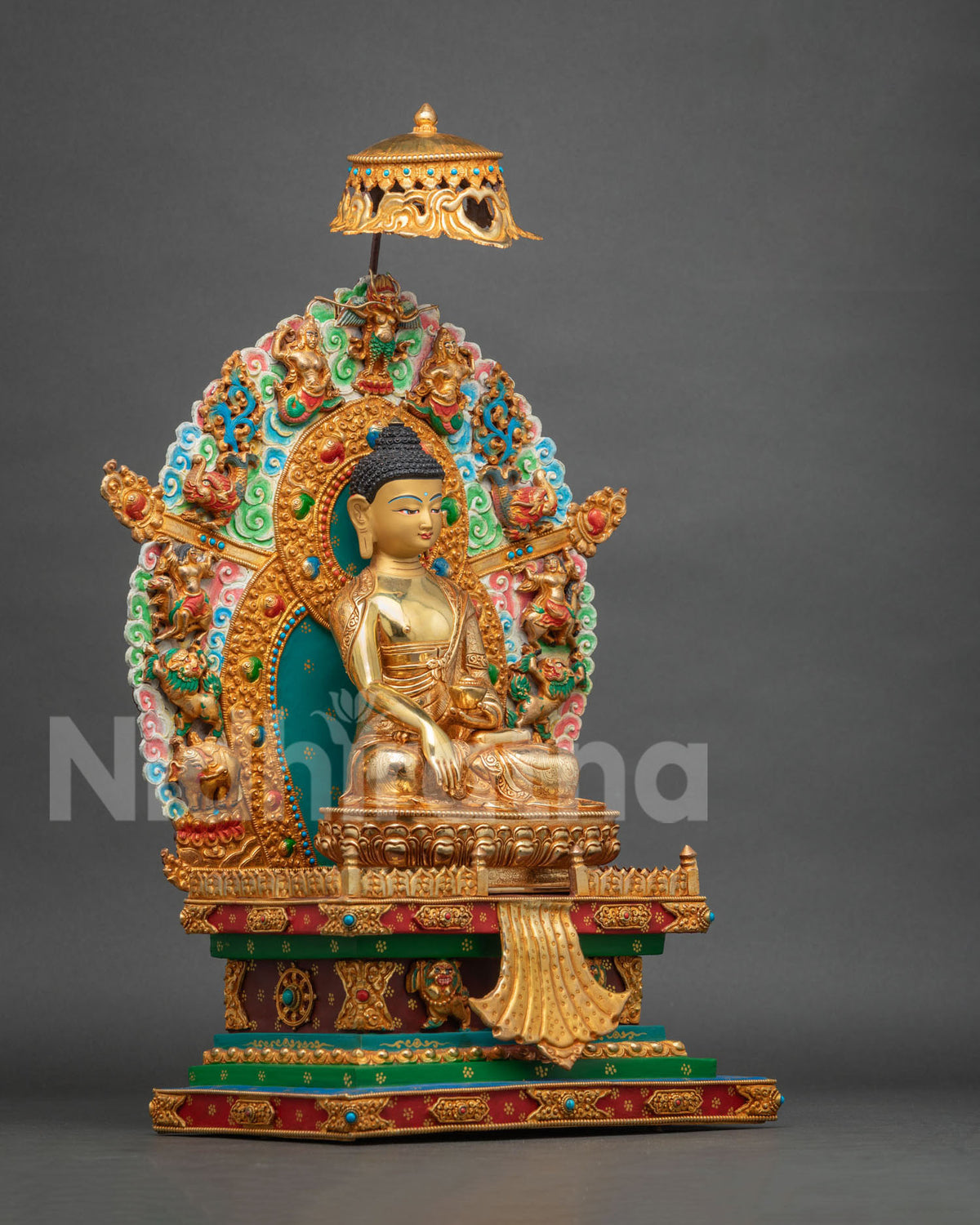 Three-quarter side view of Shakyamuni Buddha statue on throne showing gold fire-gilding and detailed halo