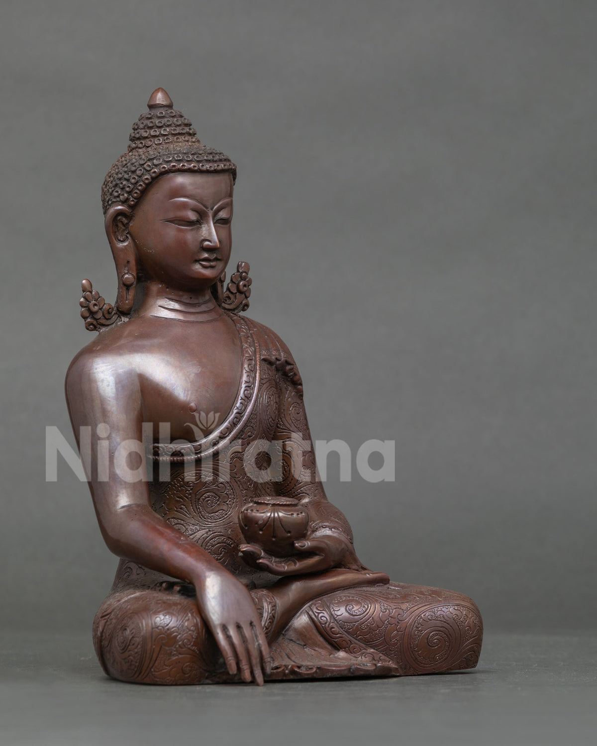 Three-quarter view of oxidized copper Shakyamuni Buddha statue holding a patra bowl