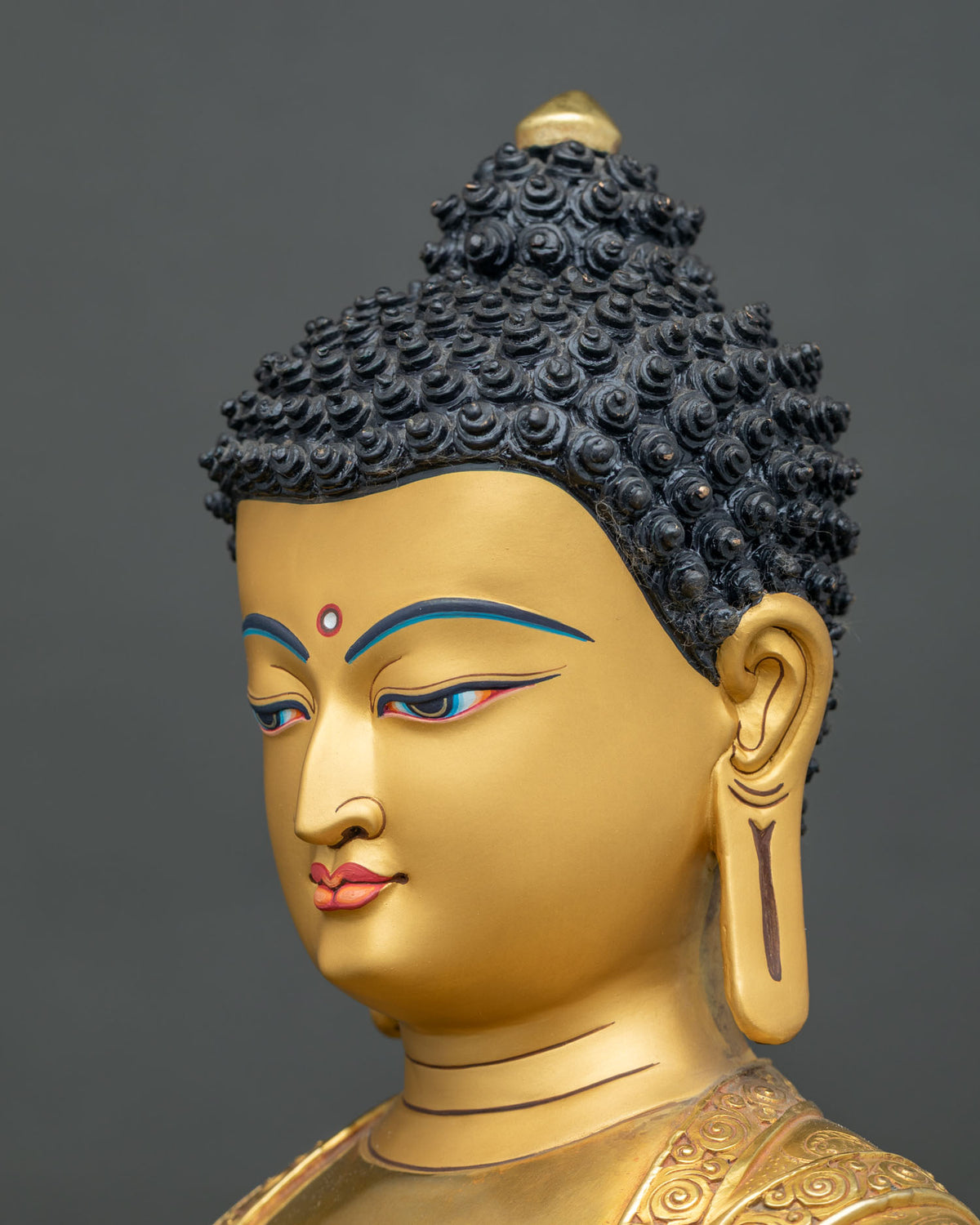 Three-quarter view of Shakyamuni Buddha statue face with gold-painted features and half-lidded gaze
