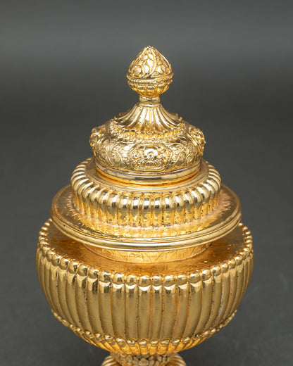 Tibetan ritual rice pot resting on sacred altar base featuring floral designs and traditional Newari metal craft detailing