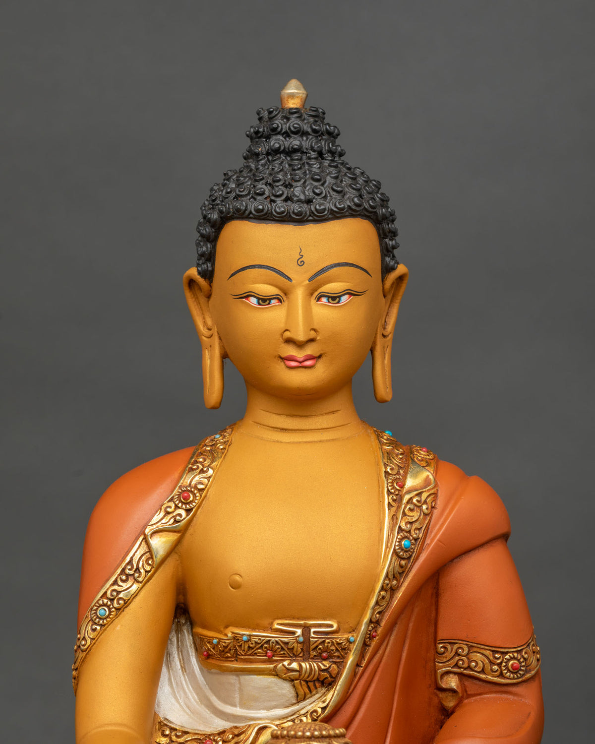 Upper body close-up of Shakyamuni Buddha statue with gold gilded robe and gemstone details