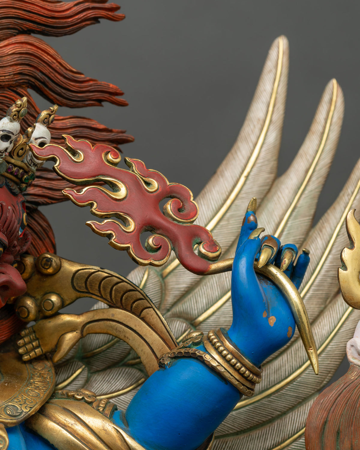 Vajrakilaya hand holding a curved gilded hook beside red flame ornament and garuda wing