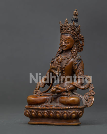 Vajrasattva statue holding vajra and bell in oxidized copper finish.