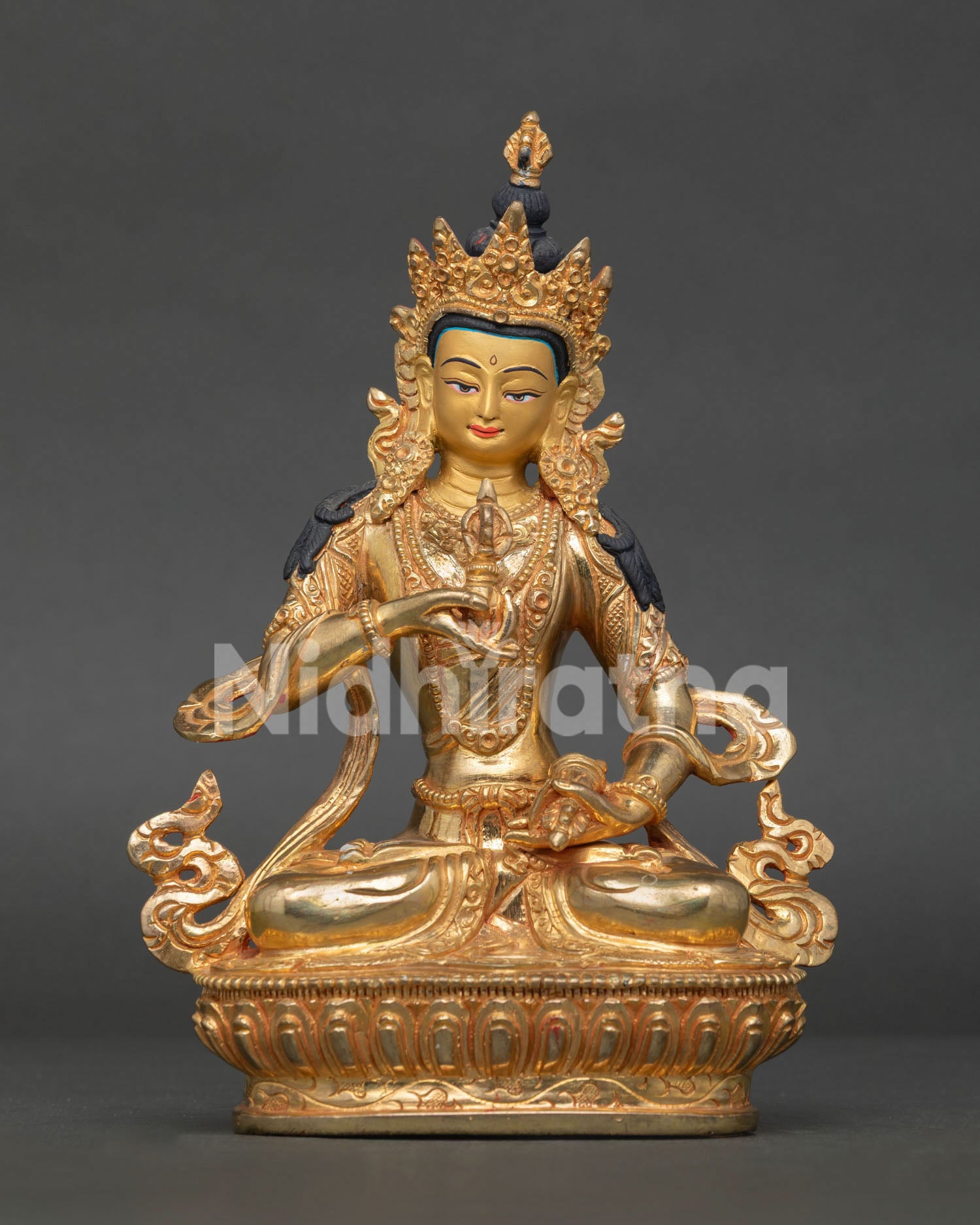 Vajrasattva statue seated on lotus pedestal holding five pronged vajra and bell.
